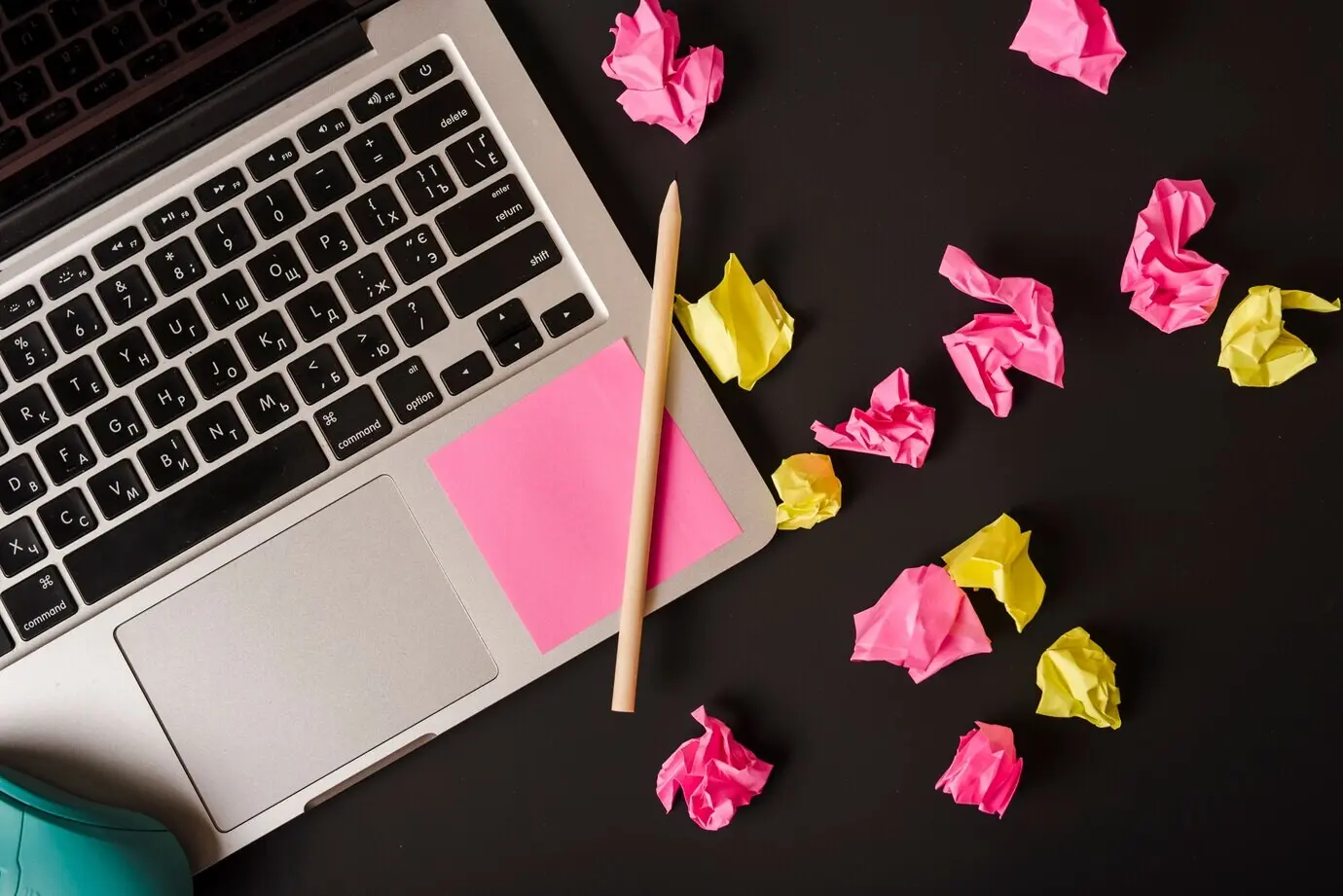 Draufsicht eines Laptops mit einem Stift und Haftnotizen vor schwarzem Hintergrund.